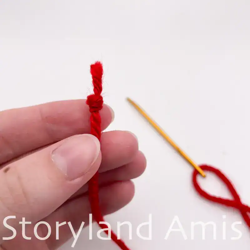 A hand holds up a length of red yarn with a knot at the end of it.