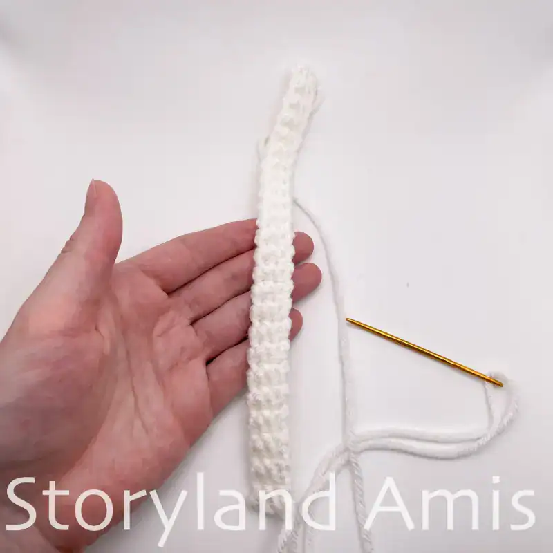 A hand holds a white, crocheted hat band for a Santa Claus hat.