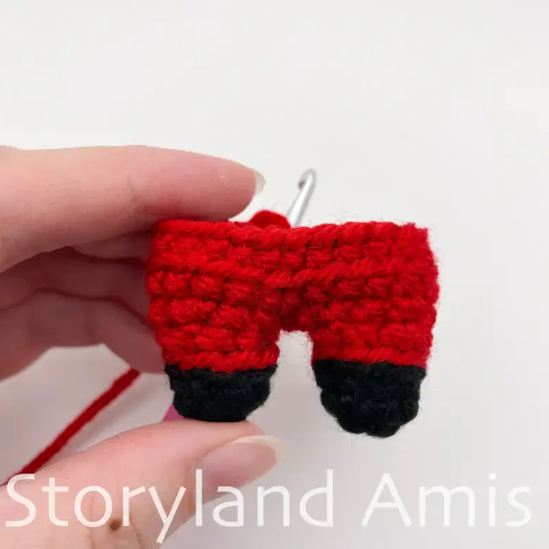A hand holds up a partially finished body for an amigurumi Santa Claus.