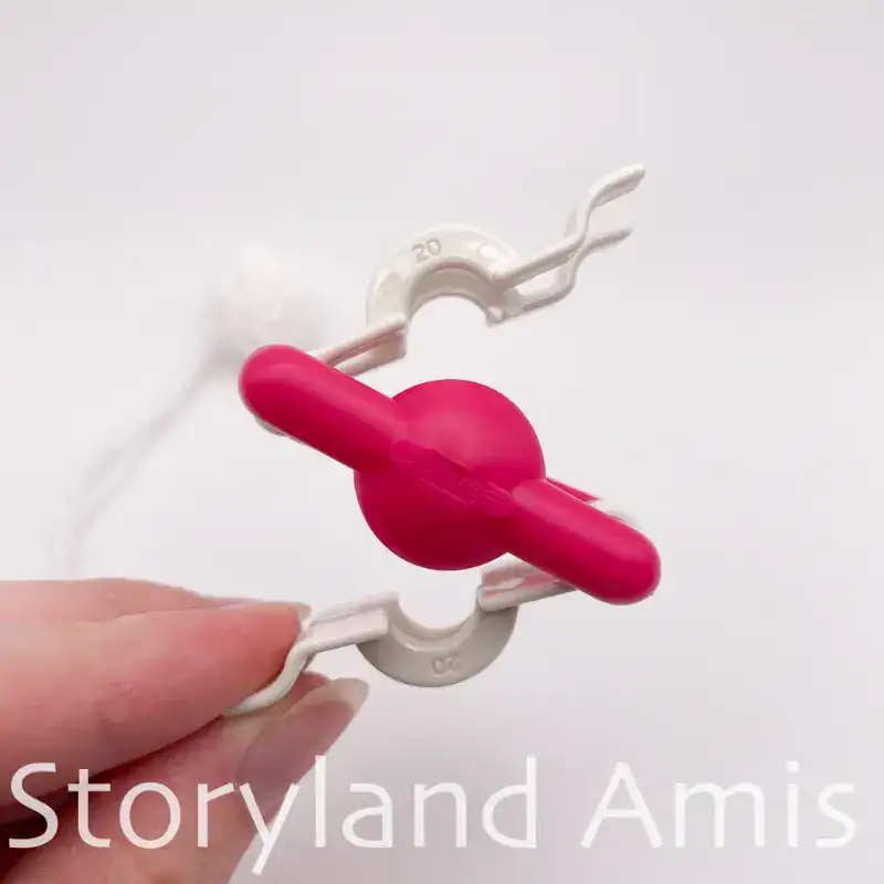 A hand holds up a pink and white pom pom maker.