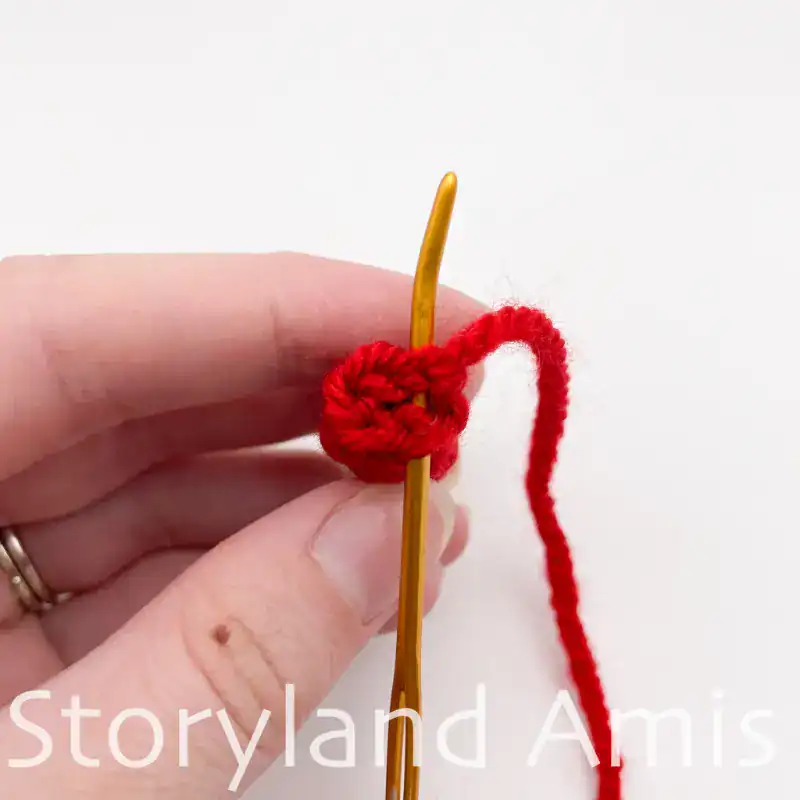 A hand uses a tapestry needle to demonstrate how to sew the open ends closed on a crocheted doll arm.