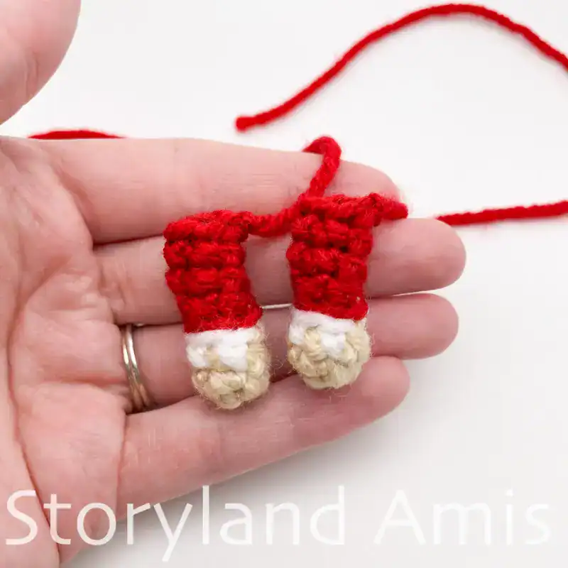A hand holds two crocheted arms for an amigurumi Santa Claus.