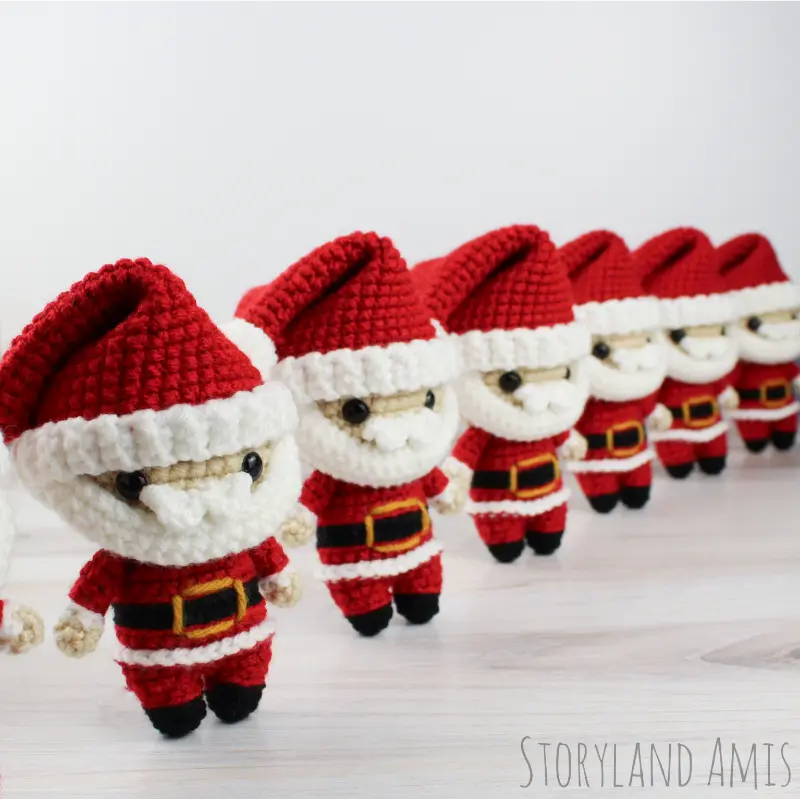 Six mini Santa Claus amigurumi dolls stand in a row on a wooden table.