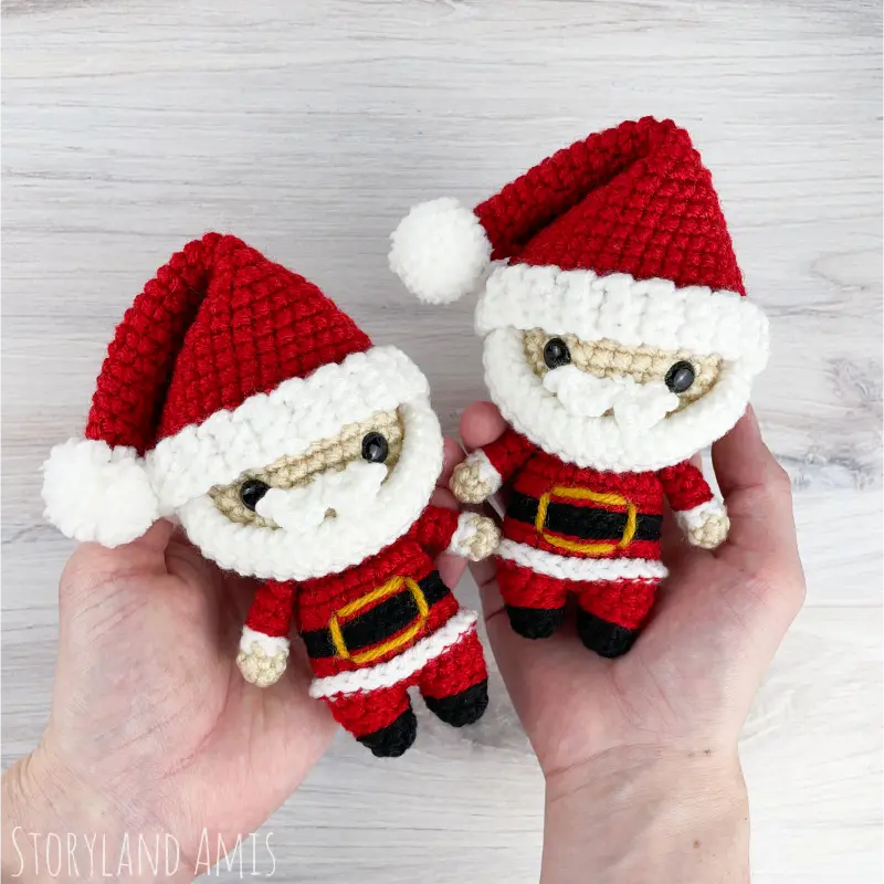 Two hands hold two mini Santa Claus amigurumi dolls.