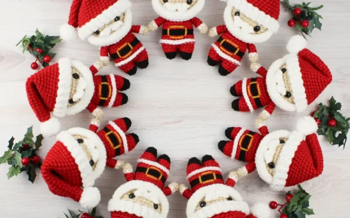 Nine mini Santa Claus amigurumi dolls lay on a wooden table arranged in a circle.