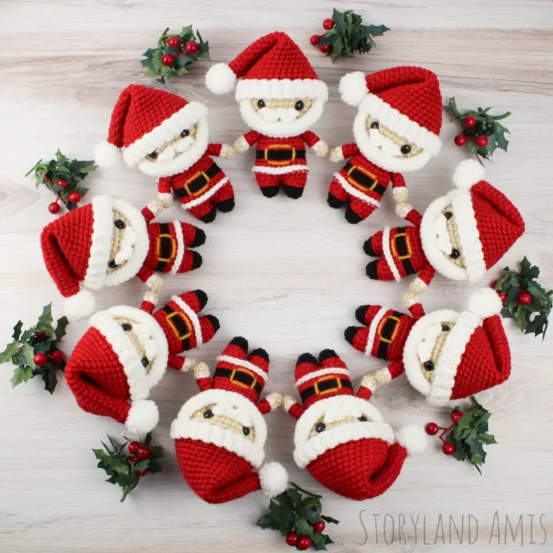 Nine mini Santa Claus amigurumi dolls lay on a wooden table arranged in a circle.