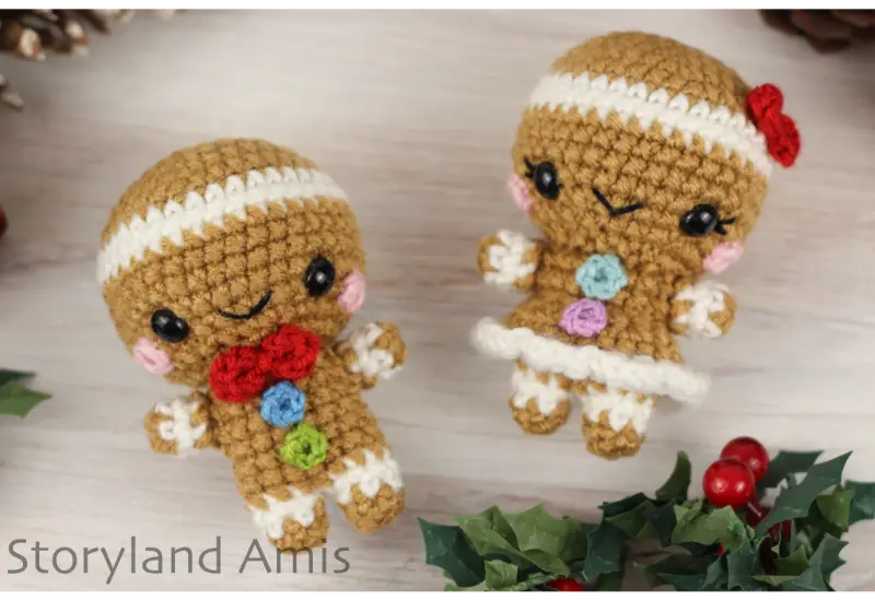An amigurumi gingerbread boy and girl lie on a wooden table.