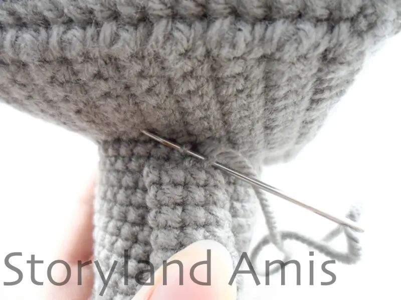 A close-up of a crocheted arm being sewn to the body of an amigurumi robot toy.