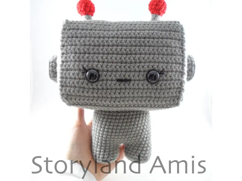 A hand holds up a partially finished amigurumi robot toy.