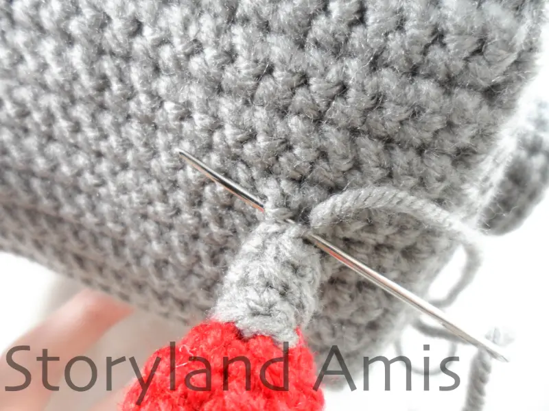 A close-up of a crocheted antenna being sewn to the top of an amigurumi robot's head.