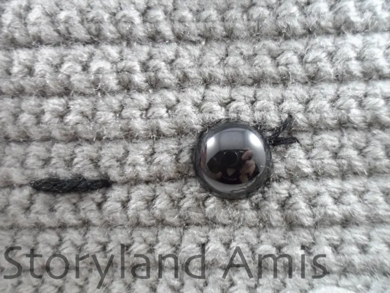 A close-up of a plastic safety eye inserted in a crocheted robot head.