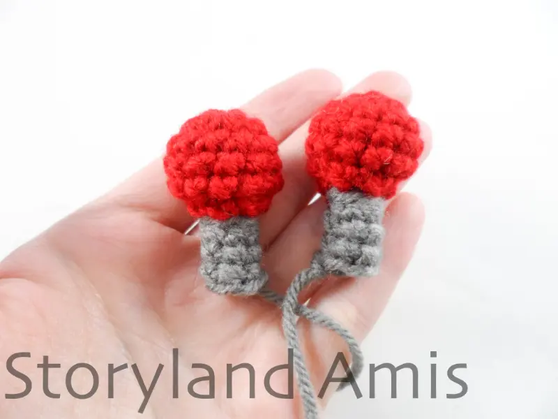 A hand holds two crocheted antennas for an amigurumi robot.