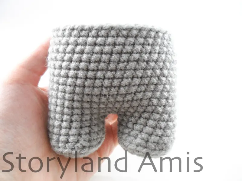 A hand holds a gray crocheted body for an amigurumi robot.