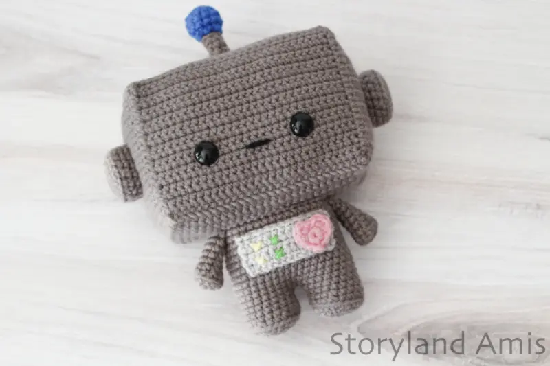 An amigurumi robot lies on a wooden table.