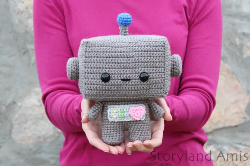 A girl holds an amigurumi robot toy in her hands.