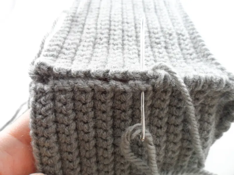 A close-up of a crocheted side panel being sewn to the side of an amigurumi robot's head.