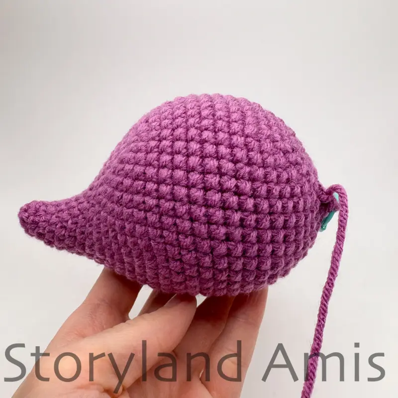 A hand holds up a partially finished amigurumi stegosaurus body.