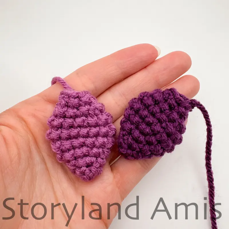 A hand holds two purple crocheted plates for an amigurumi stegosaurus.