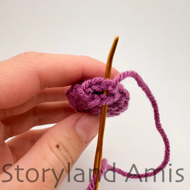 A hand demonstrates how to sew the open end closed on a crocheted piece using a tapestry needle and yarn tail.