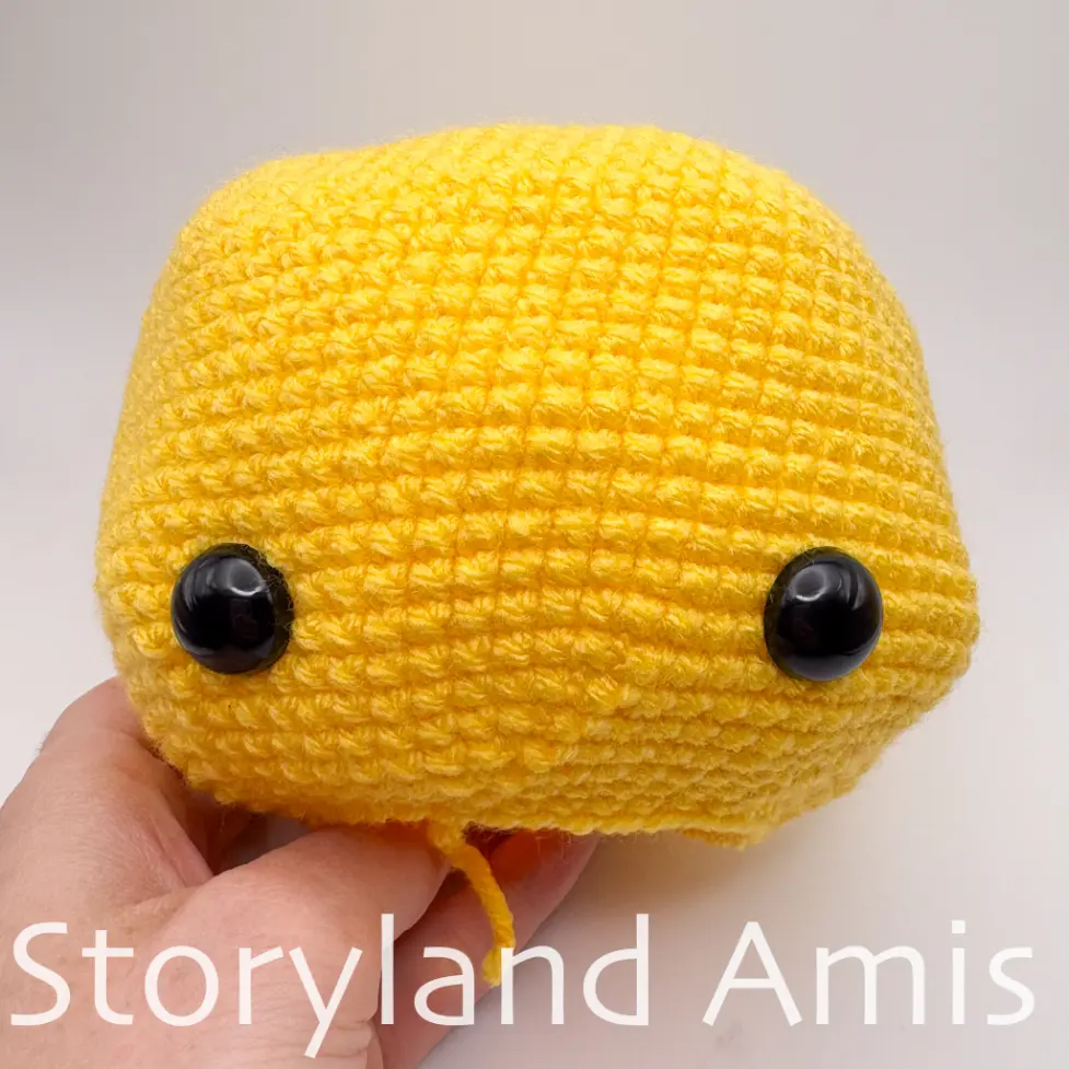 A hand holds a partially finished yellow amigurumi bumblebee head.