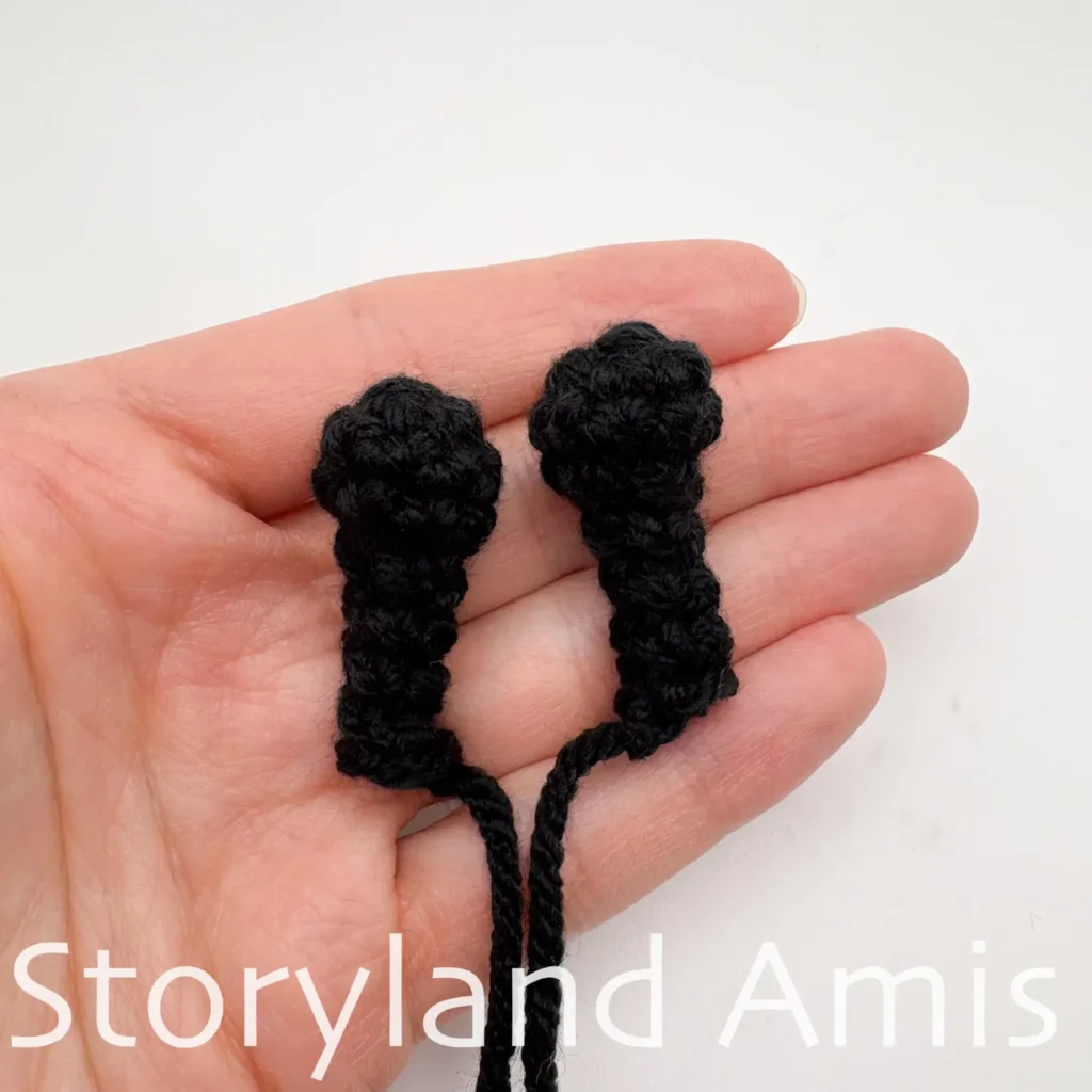 A hand holds two black crocheted antennas for an amigurumi bee.