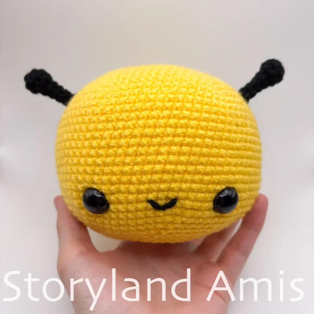 A hand holds up a crocheted bee head.