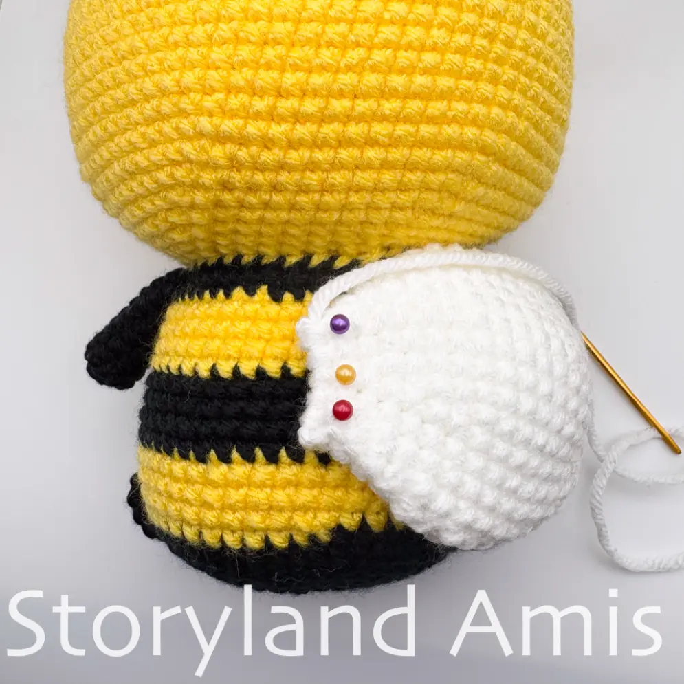 A close-up of the back of an amigurumi bee's body, showing the placement of one of the wings.