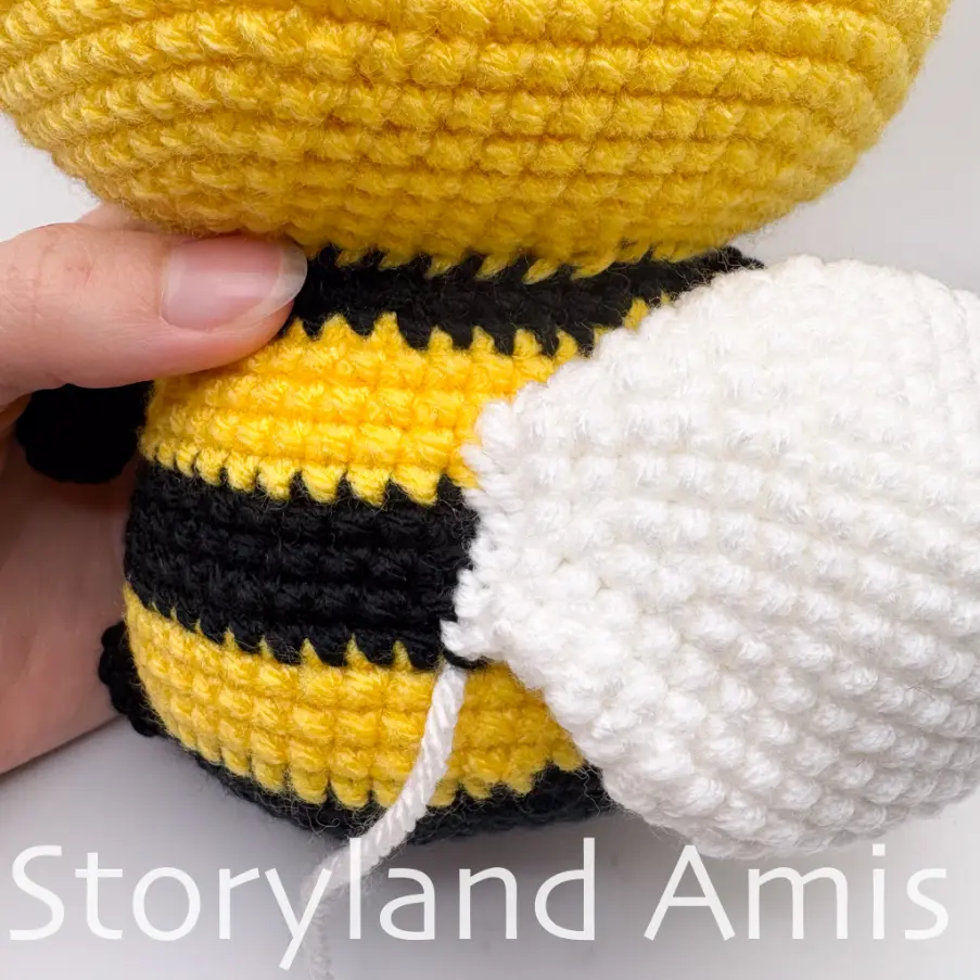 A close-up of the back of an amigurumi bee body, showing one wing sewn on.