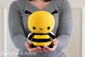 A girl wearing a gray sweater holds a large crocheted amigurumi bee.
