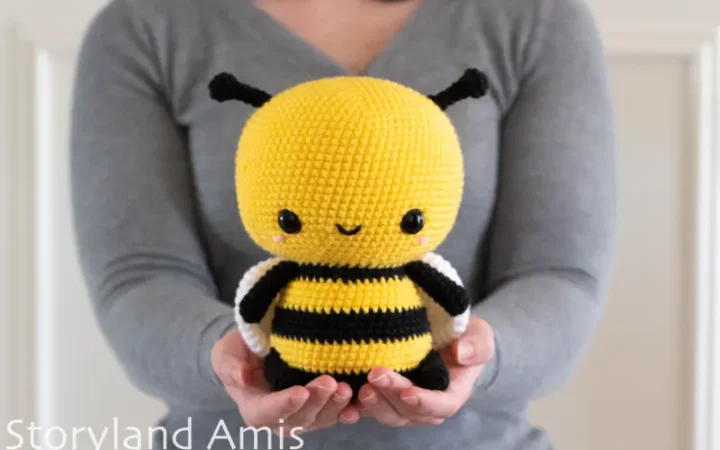 A girl wearing a gray sweater holds a large crocheted amigurumi bee.