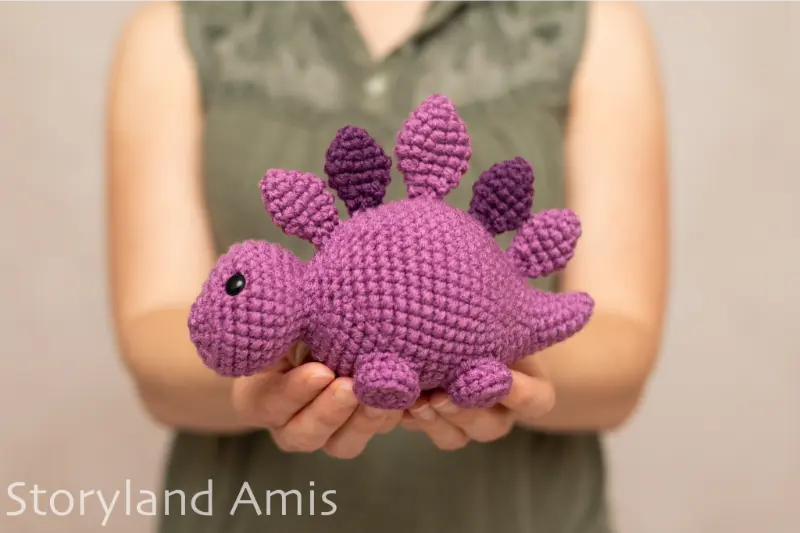A girl holds a purple crocheted stegosaurus.
