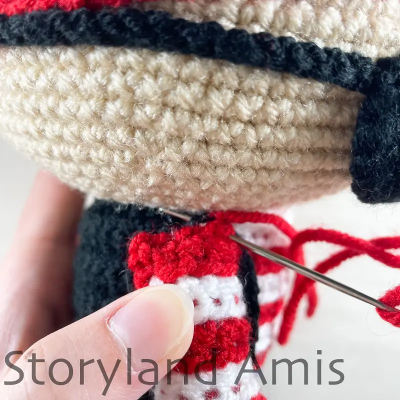 A close-up of a crocheted arm being sewn to the body of an amigurumi pirate doll using a tapestry needle.