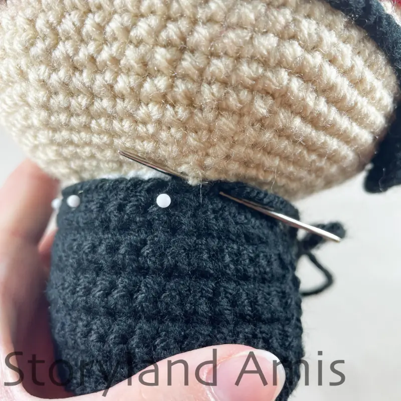 A close-up of a crocheted vest being sewn to the body of an amigurumi pirate doll using a tapestry needle.