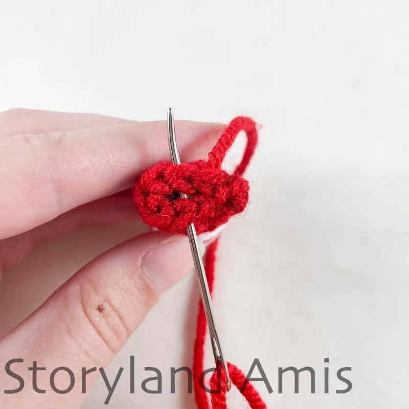 A hand holds a crocheted arm with a tapestry needle inserted in the stitches of the last round of the arm.