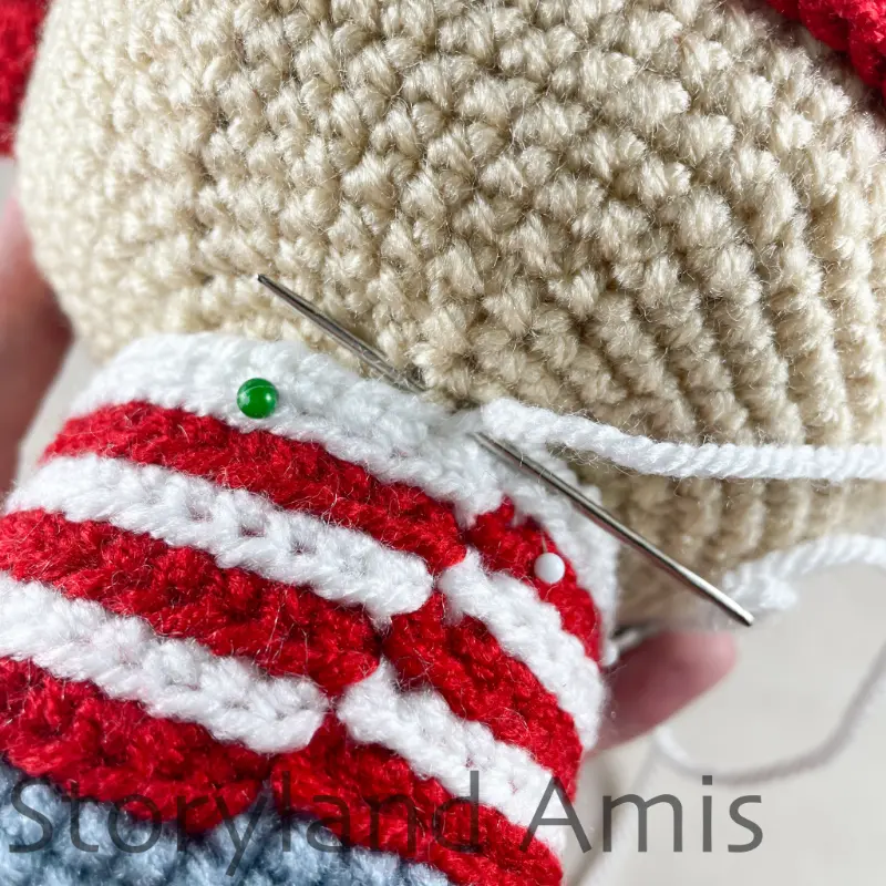 A close-up of a crocheted body being sewn to the head of an amigurumi pirate doll.