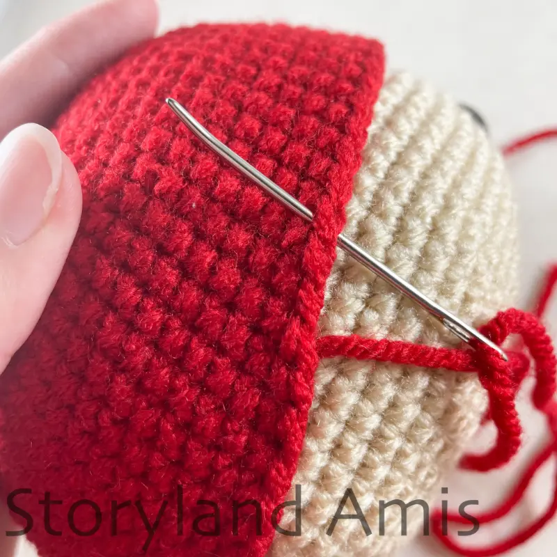 A close-up showing how to sew a crocheted hat to an amigurumi pirate's head using a tapestry needle.
