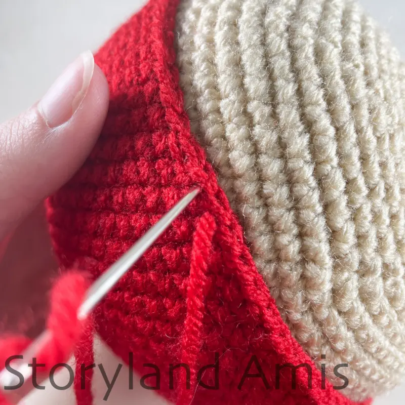 A close-up showing how to sew a crocheted hat to an amigurumi pirate's head using a tapestry needle.