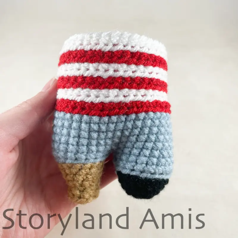 A hand holds up a crocheted doll's body.