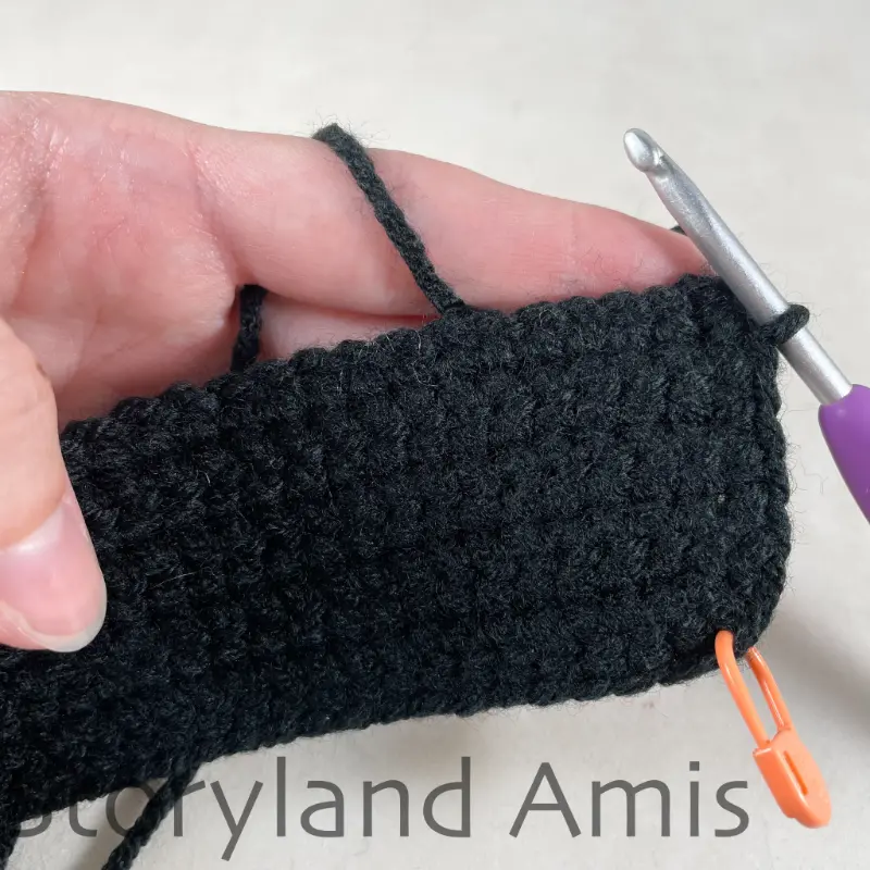 A close-up of a border being crocheted along the edges of a small black crocheted vest for an amigurumi pirate doll.