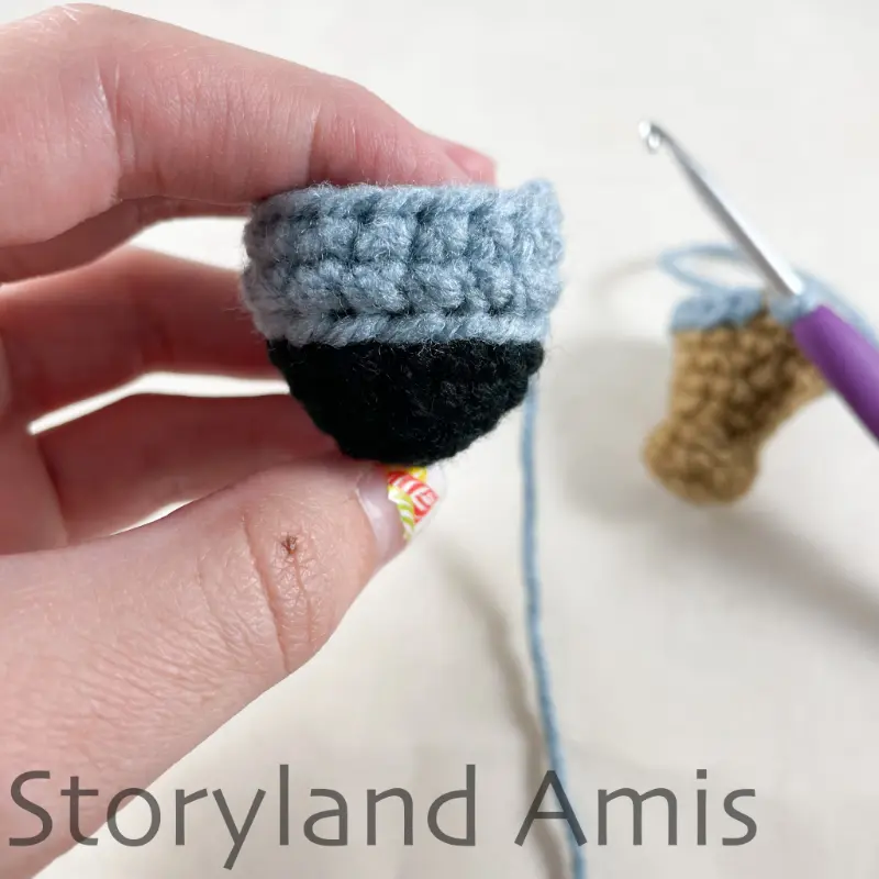 A hand holds up a crocheted leg for an amigurumi pirate doll.