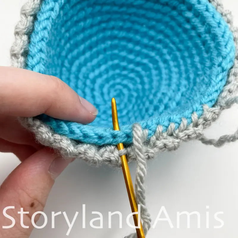 A close-up of a hand demonstrating how to sew a hat band around the bottom edge of a crocheted hat for an amigurumi snowman.