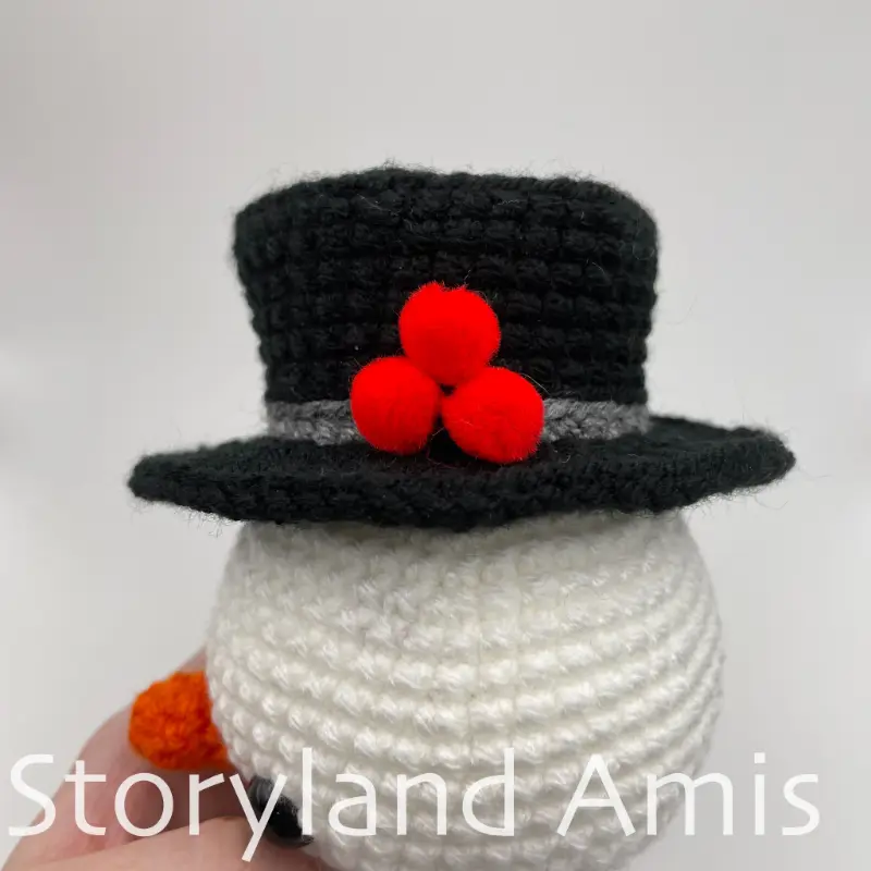 A close-up of a crocheted top hat on an amigurumi snowman's head, shown from the side.