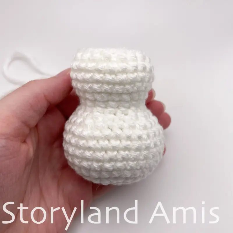 A hand holds a white, crocheted snowman body.