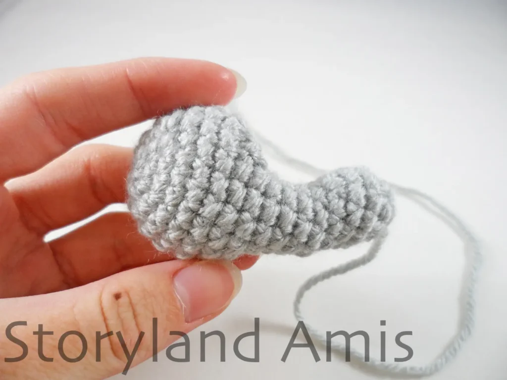 A hand holds up a gray crocheted koala leg.
