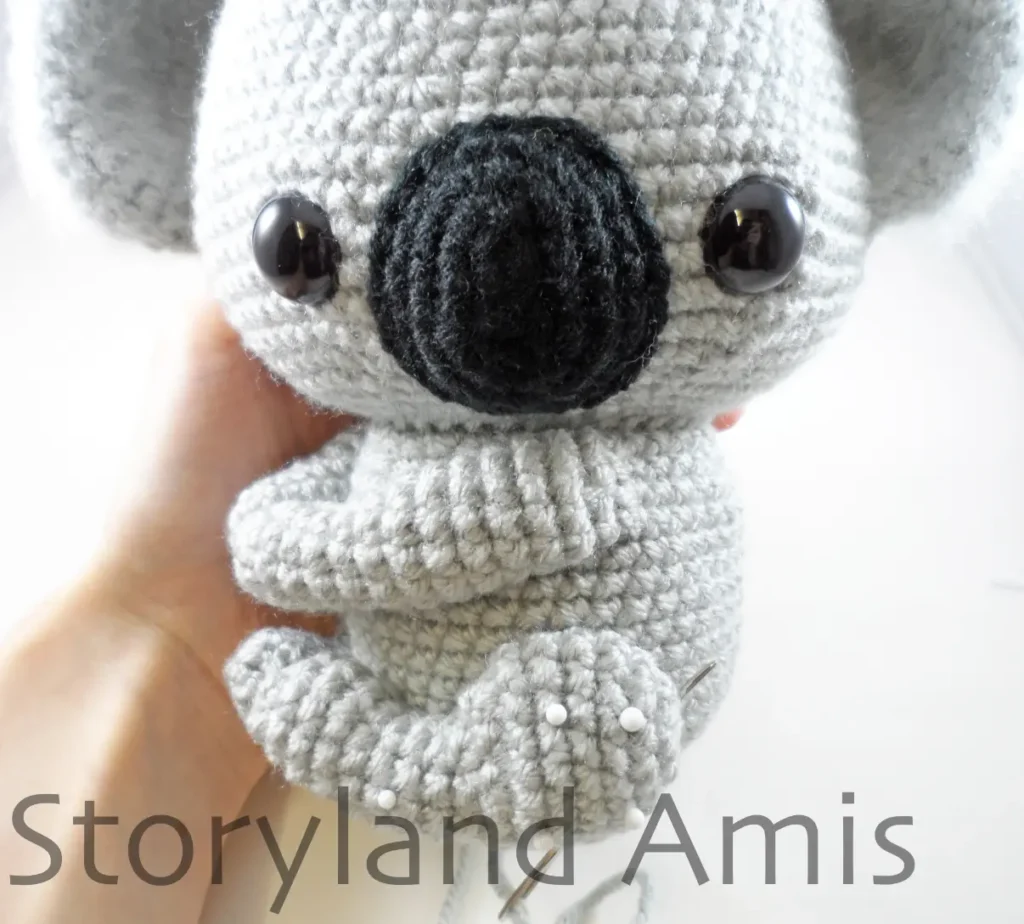 A hand holds a partially finished amigurumi koala.