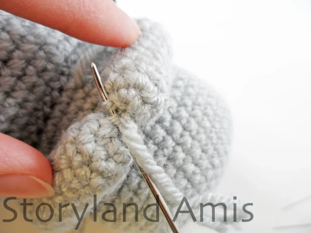 A close-up of tips of two crocheted koala arms being sewn together using a tapestry needle and yarn tail.