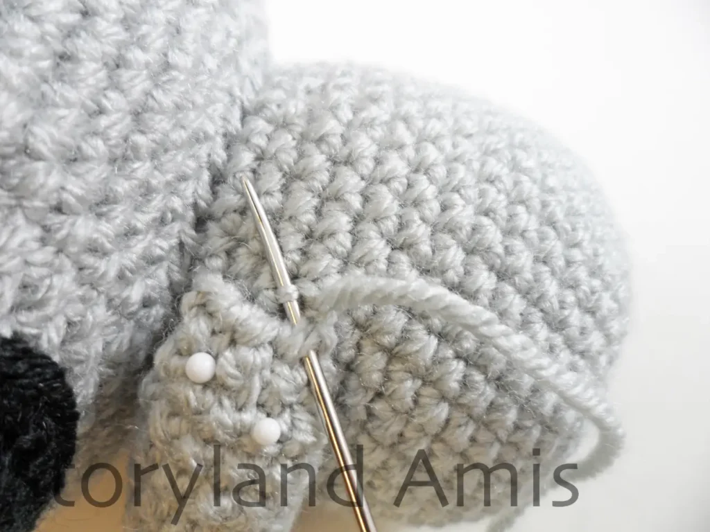 A close up of a crocheted arm being sewn to the side of an amigurumi koala's body using a tapestry needle. 