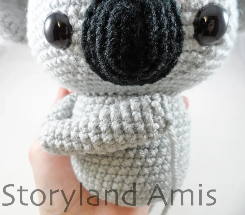 A close-up of a crocheted koala's body with an arm pinned to the front of the body.