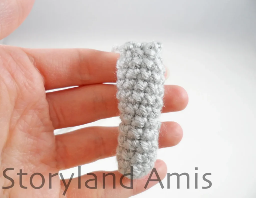 A hand holds a crocheted arm for an amigurumi koala.