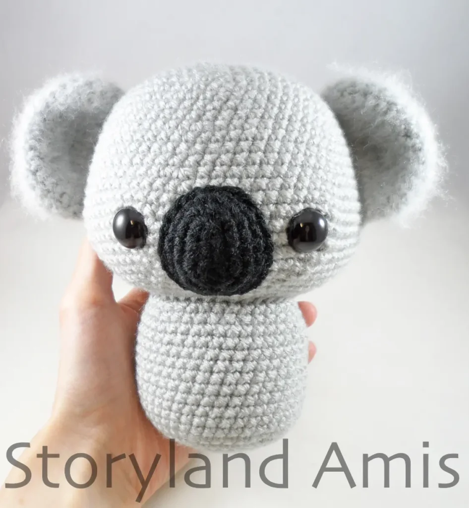 A hand holds up a work-in-progress amigurumi koala.